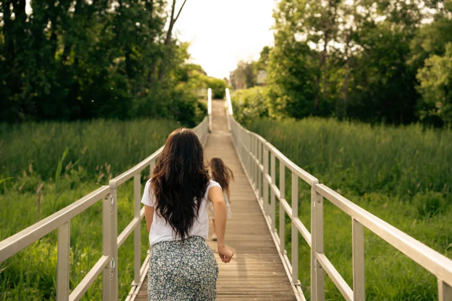 Madre e hija corriendo por una pasarela de madera en un parque natural